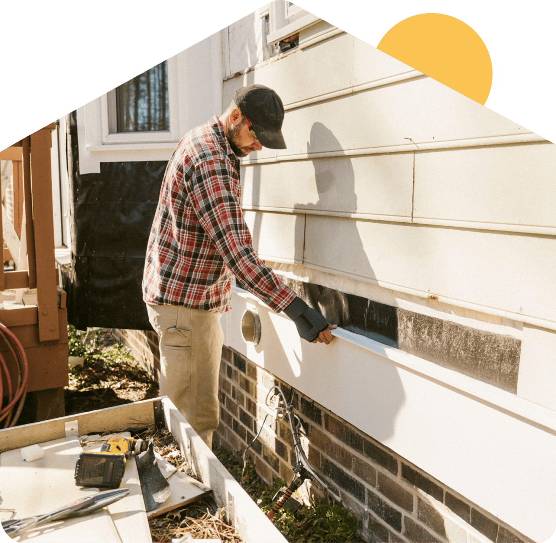 Man installing siding on a house exterior.